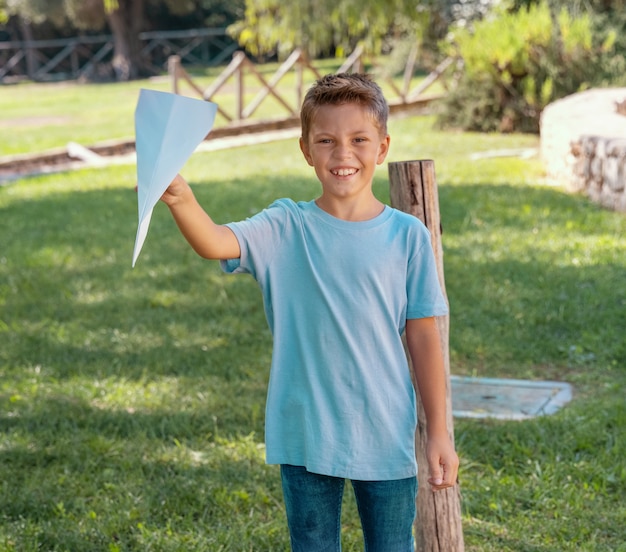 Niño feliz en edad preescolar juega con un avión de papel en un parque