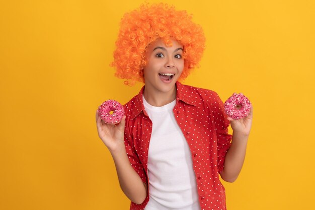 Niño feliz con una elegante peluca naranja, cabello, dulce rosquilla glaseada, felicidad