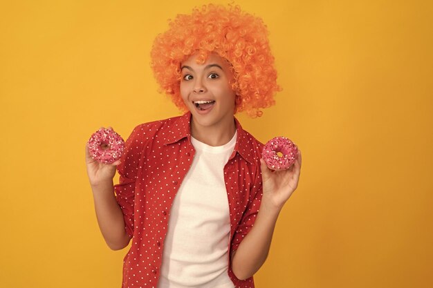 Niño feliz con una elegante peluca naranja, cabello, dulce rosquilla glaseada, felicidad