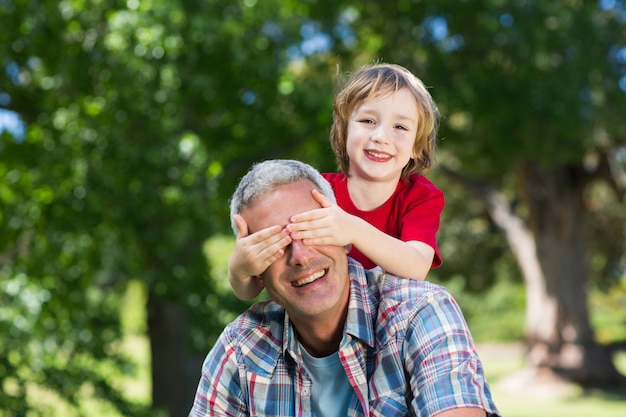 Foto niño feliz escondiendo los ojos de su padre con las manos