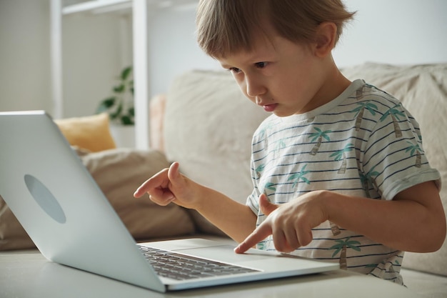 Niño feliz escribiendo usando una computadora portátil sentada en un sofá en casa Educación remota en casa