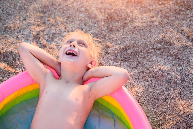 Niño feliz está acostado en la piscina para niños con las manos detrás de la cabeza y mira al cielo