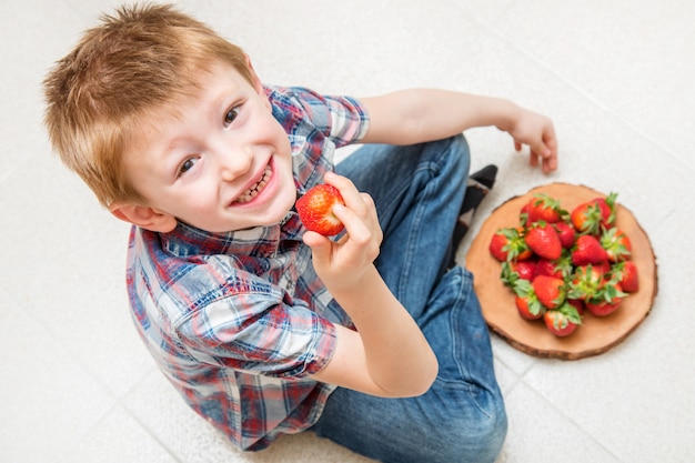 niño feliz está comiendo fresas frescas