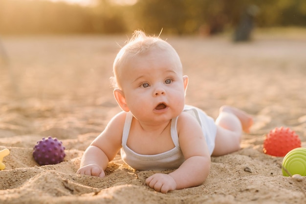 Un niño feliz está tumbado en una playa de arena cerca del mar bajo los rayos del sol poniente