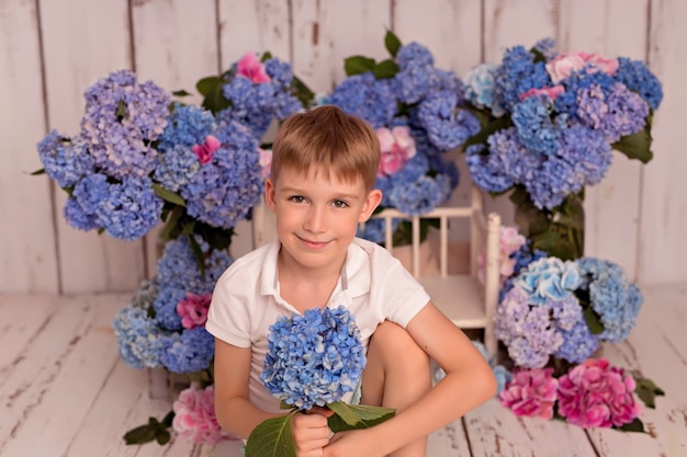 Niño feliz en el estudio sobre un fondo blanco con flores de hortensias rosas y azules