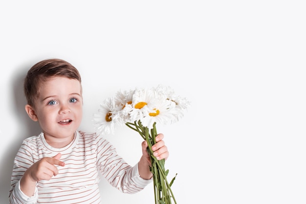 Un niño feliz con flores de margarita en el fondo blanco, un lindo niño sonriente se divierte en el verano