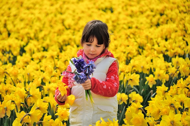 Niño feliz con flores de primavera en campo de narcisos amarillos, niña en viaje de vacaciones en Holanda