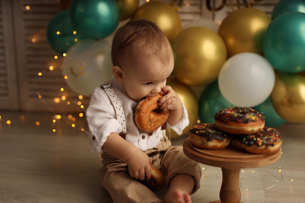 Un niño feliz en el fondo de globos con guirnaldas come donuts de chocolate Feliz cumpleaños