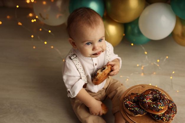 Un niño feliz en el fondo de globos con guirnaldas come donuts de chocolate Feliz cumpleaños