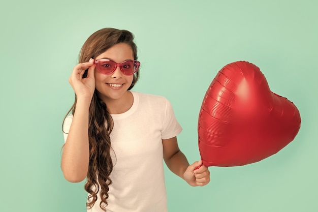 Niño feliz con gafas de sol sostiene un globo de fiesta de corazón rojo para el día de san valentín símbolo de amor día de amor