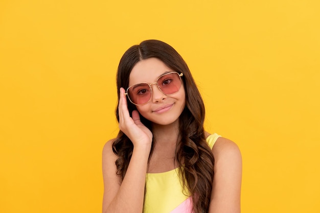 Niño feliz en gafas de verano tiene el pelo rizado sobre fondo amarillo, belleza.