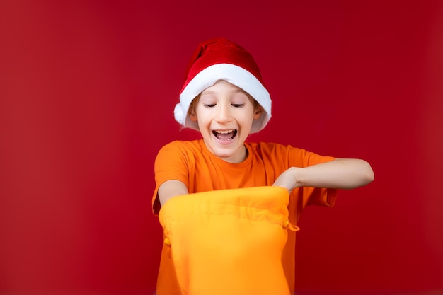 Un niño feliz con un gorro de Papá Noel metió la mano en una bolsa de regalo amarilla