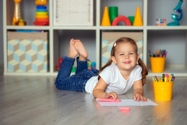 niño feliz en la guardería y dibuja en papel con marcadores de colores