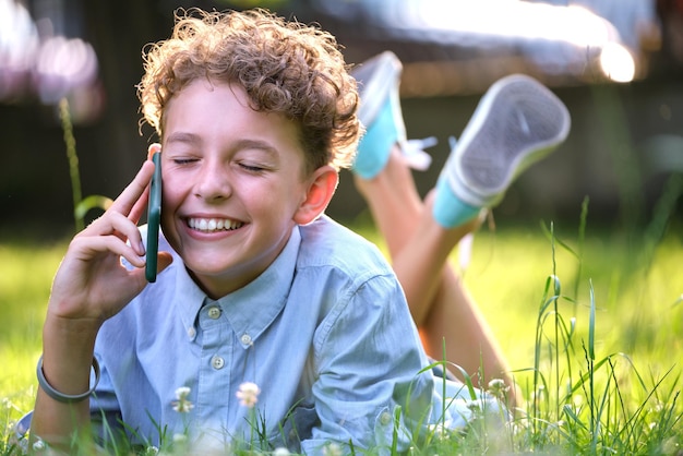 Niño feliz hablando por celular al aire libre en el parque de verano