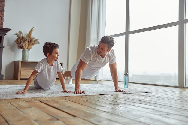 Niño feliz haciendo flexiones con el padre en casa