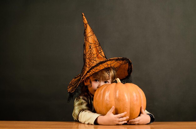 Niño feliz de halloween jugando truco o trato niño con sombrero de bruja escondido en la calabaza de halloween