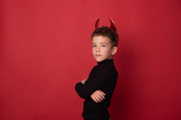 Niño feliz de Halloween se ríe a carcajadas con cuernos diabólicos contra un fondo rojo del estudio