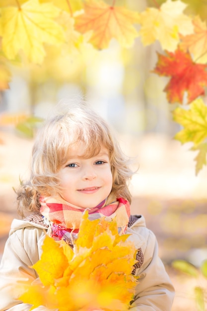 Niño feliz con hojas de arce en el parque otoño