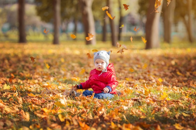 Niño feliz y hojas caídas jugando en el parque otoño