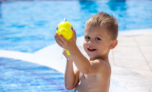 Niño feliz juega en la piscina con un enfoque selectivo de pistola de agua
