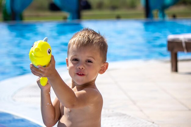 Niño feliz juega en la piscina con un enfoque selectivo de pistola de agua