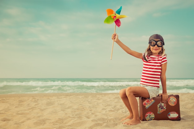 Foto niño feliz jugando con aerogeneradores de juguete contra el mar y el cielo piloto de niño divirtiéndose al aire libre vacaciones de verano y concepto de viaje libertad e imaginación