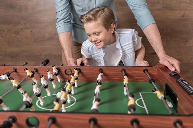 Niño feliz jugando al futbolín junto con el padre