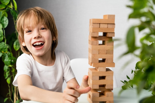 Foto niño feliz jugando al juego de mesa construyendo una torre de cubos de madera juego de lógica jenga para el desarrollo infantil