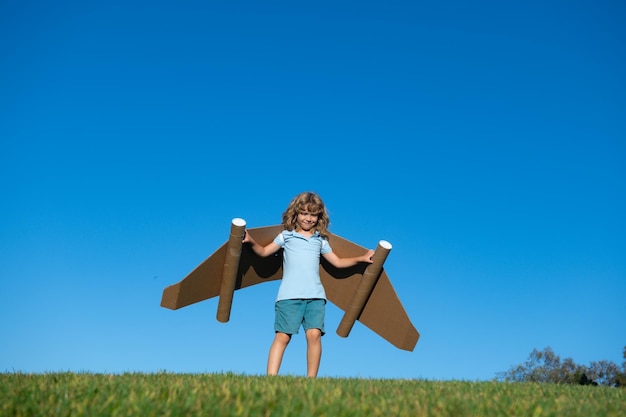 Niño feliz jugando con alas de juguete contra el fondo del cielo de verano Concepto de ganador y líder de éxito de los niños