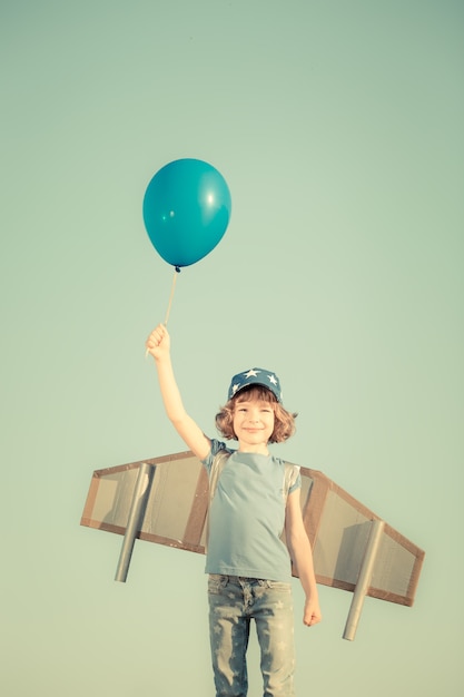 Niño feliz jugando con alas de juguete contra el fondo del cielo de verano. Tonos retro