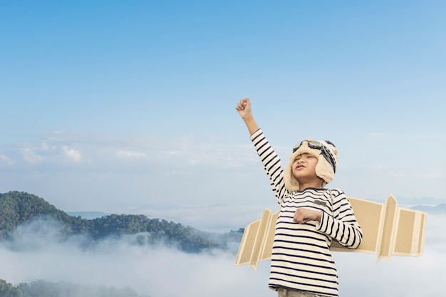 Foto niño feliz jugando con alas de juguete contra el fondo del cielo de verano.