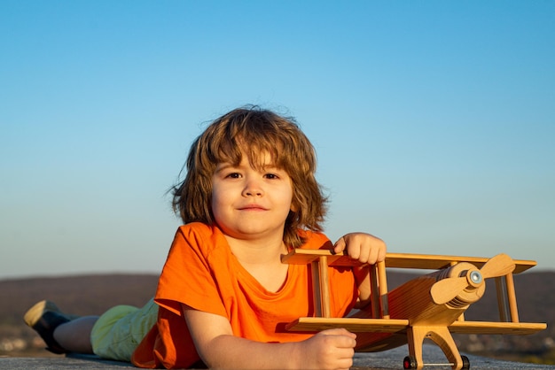 Niño feliz jugando con un avión de juguete contra el fondo del cielo azul lindo niño caminando en un verano soleado