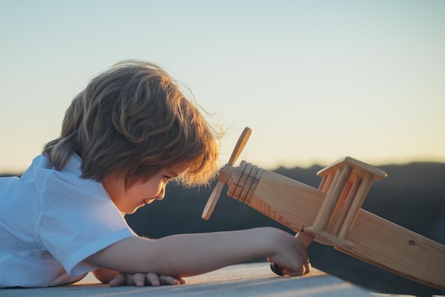 Niño feliz jugando con un avión de juguete contra el fondo del cielo azul lindo niño caminando en un verano soleado