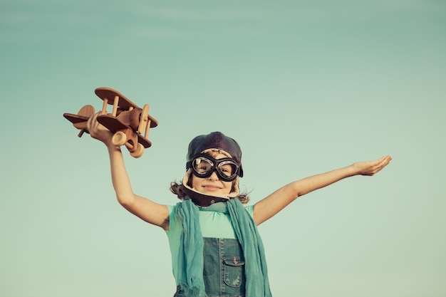 Foto niño feliz jugando con un avión de juguete contra el fondo del cielo de verano tonos retro