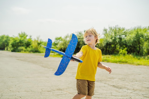 Niño feliz jugando con un avión de juguete contra el fondo de la pista antigua Viajando con el concepto de niños