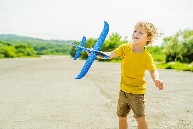 Niño feliz jugando con un avión de juguete contra el fondo de la pista antigua Viajando con el concepto de niños