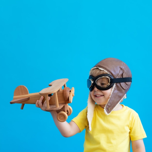 Foto niño feliz jugando con avión de madera vintage contra la pared azul.