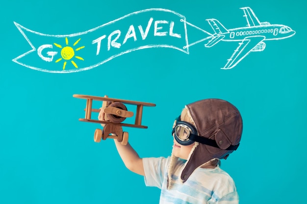 Niño feliz jugando con avión de madera vintage contra la pared azul.