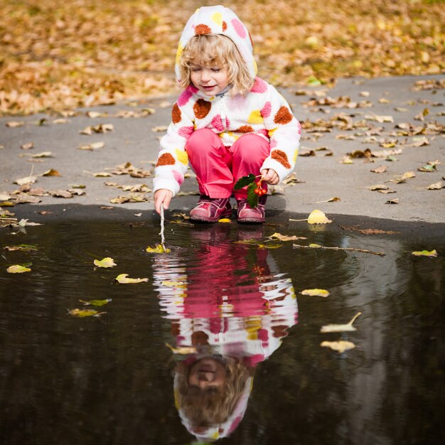 Niño feliz jugando en charco en el parque otoño