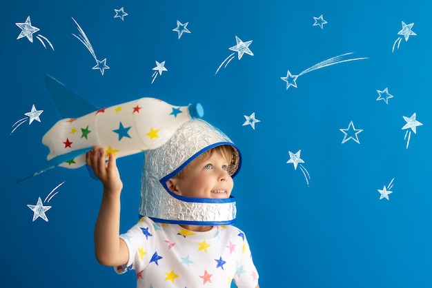 Niño feliz jugando con cohete de juguete contra el fondo azul Kid pretende ser astronauta Imaginación y concepto de sueño de los niños