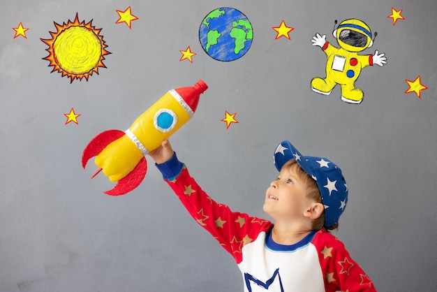 Niño feliz jugando con cohete de juguete contra el fondo de la pared de hormigón Kid pretende ser astronauta Imaginación y concepto de sueño de los niños