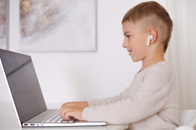 Niño feliz jugando en la computadora portátil en casa. Retrato de un niño en casa viendo dibujos animados en la computadora. Tecnología moderna para niños y educación.