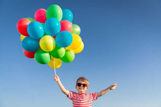 Niño feliz jugando con globos multicolores brillantes al aire libre