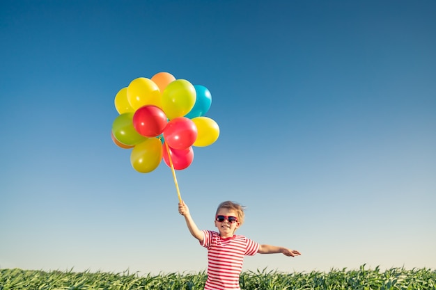 Niño feliz jugando con globos multicolores brillantes al aire libre.