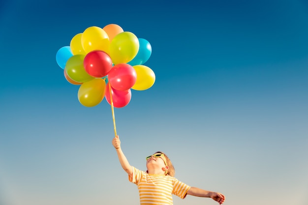 Niño feliz jugando con globos multicolores brillantes al aire libre.