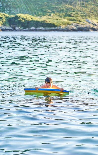 Niño feliz jugando en el mar con bodyboard. Niño divirtiéndose al aire libre. Concepto de vacaciones de verano y estilo de vida saludable.