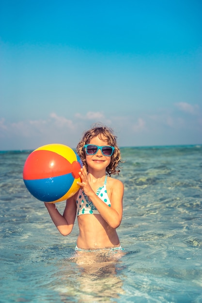 niño feliz jugando en el mar con una colorida pelota inflable