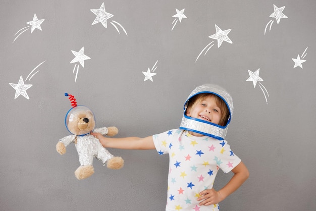 Niño feliz jugando con osito de peluche en casa Niño finge ser astronauta Imaginación y concepto de sueño infantil