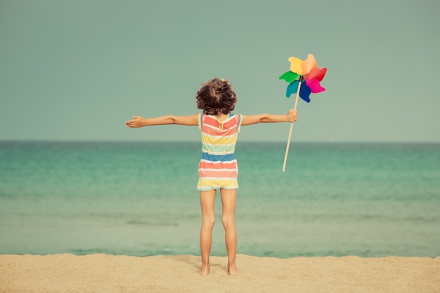 Foto niño feliz jugando en la playa con un molinete contra el fondo del cielo y el mar