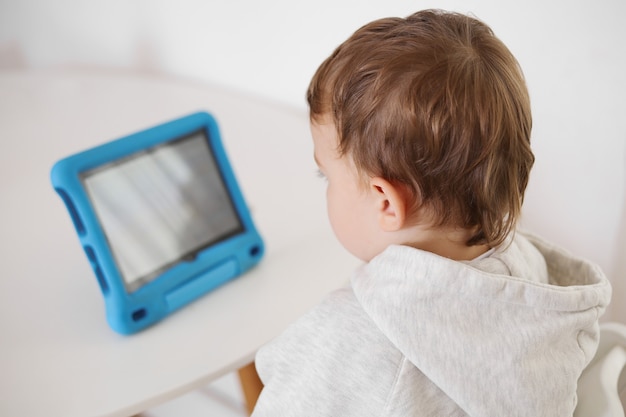 Foto niño feliz jugando en tableta digital en casa. retrato de un niño en casa viendo dibujos animados en la tableta. tecnología moderna para niños y educación.